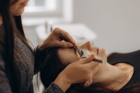 Beautician applying artificial eyelashes with tweezers on a client's eye, focusing on beauty and cosmetic procedures
