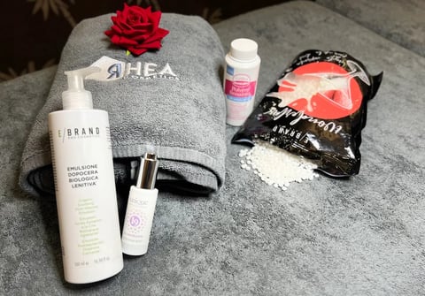 Flatlay of beauty and skincare products including cleansers, serums, and face masks arranged on a gray towel with a red rose