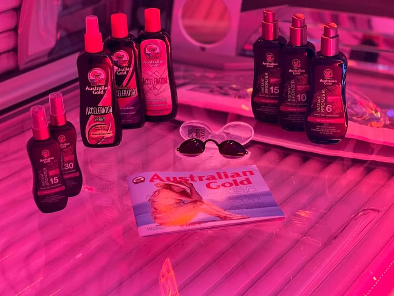 Collection of Australian Gold sunscreen bottles and sunglasses arranged on a pink tanning bed with product brochure
