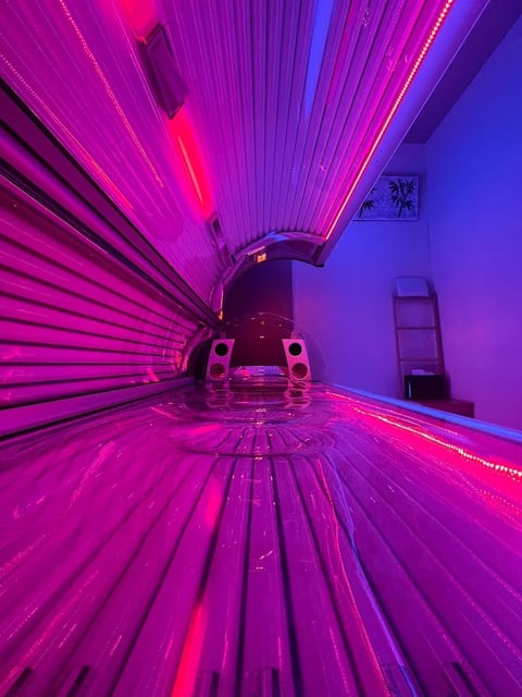 Interior view of a tanning bed with neon pink and blue lights, showing the sunbeds ribbed panels and control mechanism