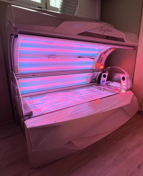 Pink and blue neon-lit tanning bed with open acrylic hood in an indoor room